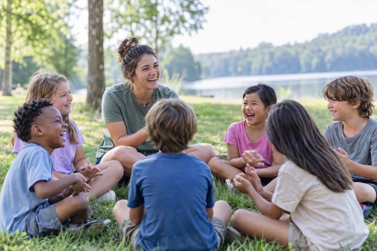 Kids laughing in a circle on the grass with a camp counselor